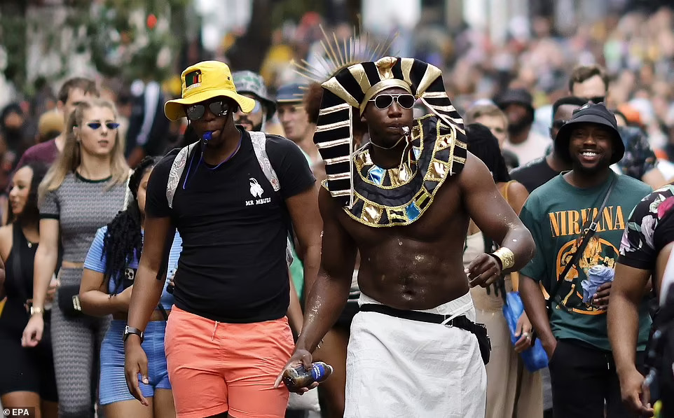 A carnival reveler wears a pharaoh outfit with a whistle in his mouth as thousands walk the streets of the west London in notting hill carnival 2022